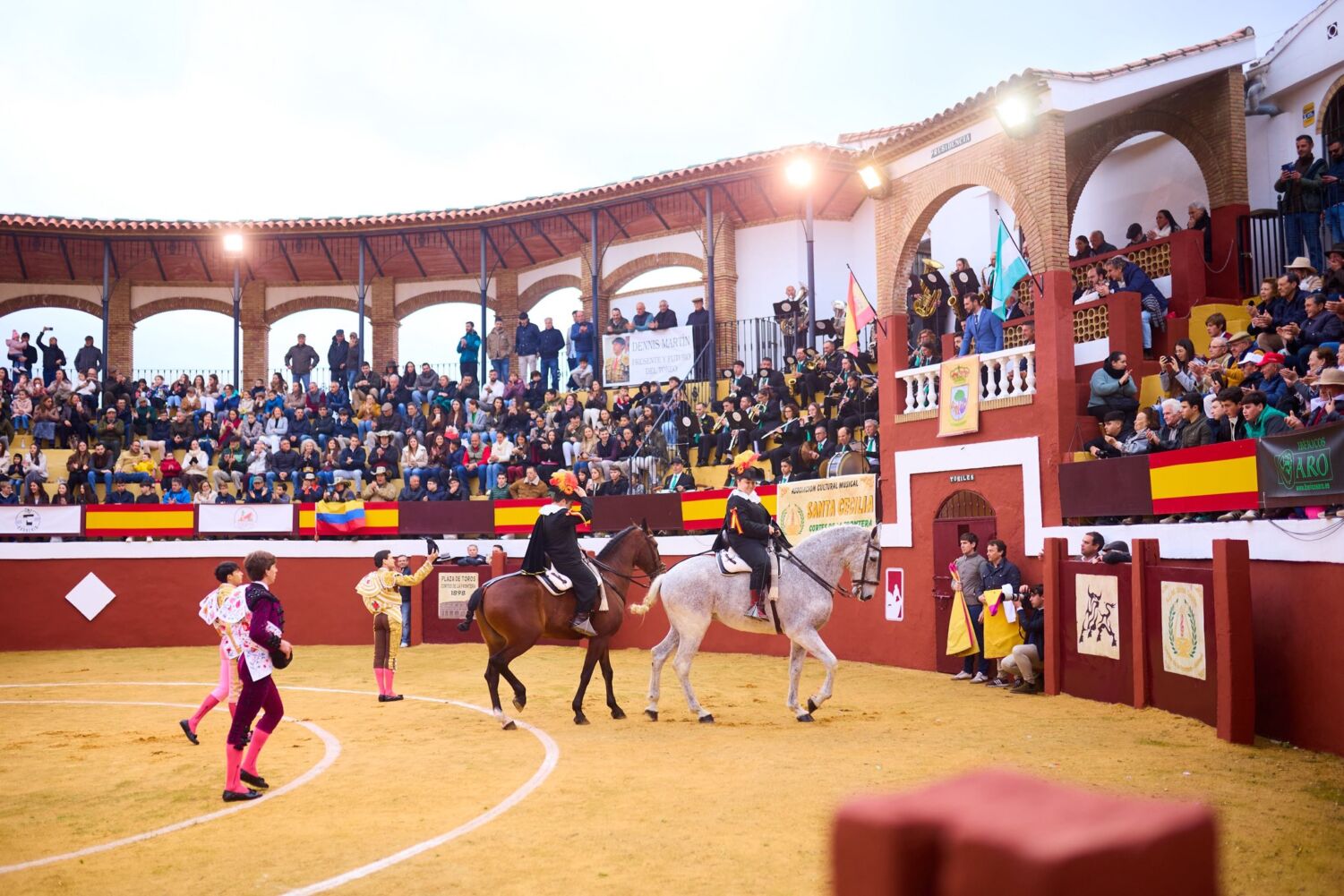 Ambiente festivo en la Plaza de Toros de Cortes de la Frontera durante la Feria de Agosto, con las gradas llenas de público y el ambiente de las fiestas patronales de San Roque y San Sebastián